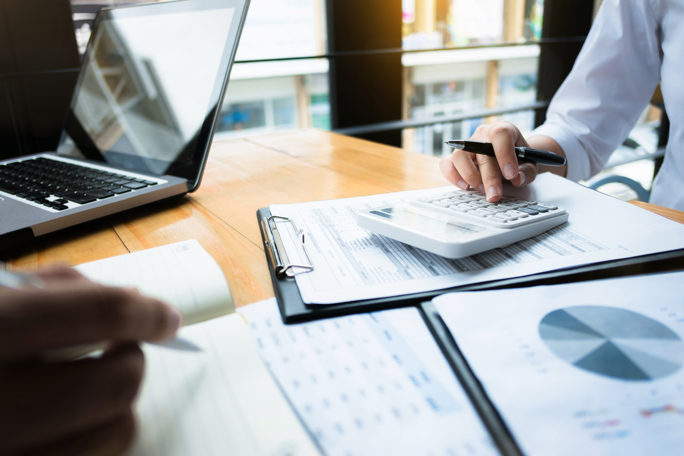 Two people are working at a wooden desk during a business meeting or financial review.