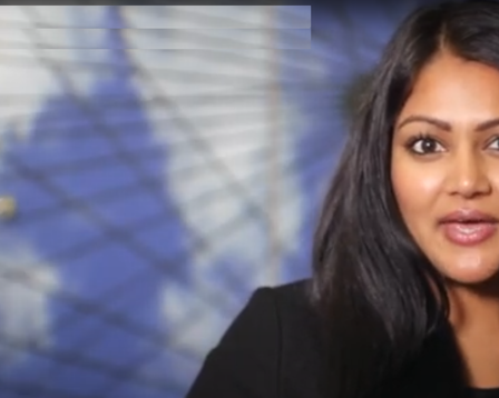 A woman with long, dark hair and medium skin tone is speaking or presenting indoors.