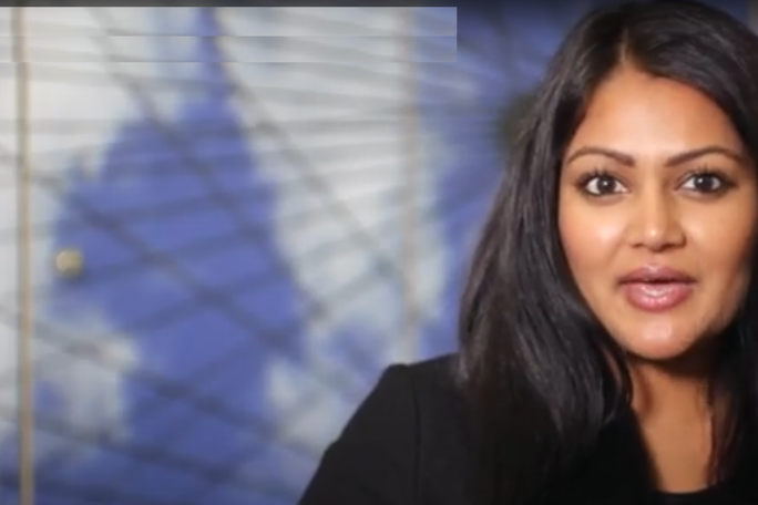 A woman with long, dark hair and medium skin tone is speaking or presenting indoors.