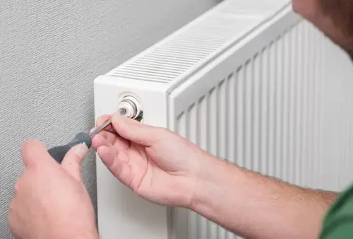 Close-up of hands bleeding a radiator with a screwdriver for winter heating maintenance
