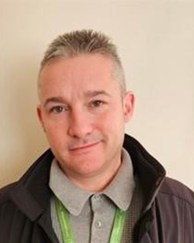 A headshot of a mature male apprentice wearing a grey t shirt and a black jacket