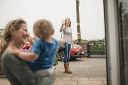 Women waves goodbye to her mother and son from across the street as she leaves the house.