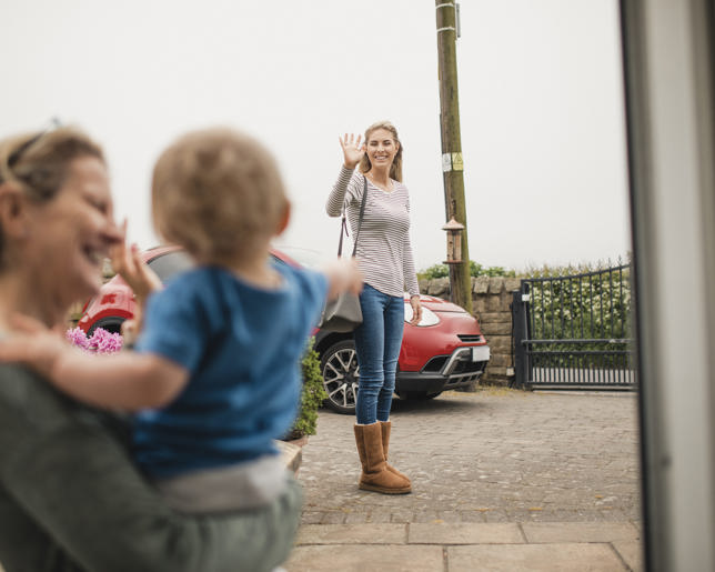Women waves goodbye to her mother and son from across the street as she leaves the house.