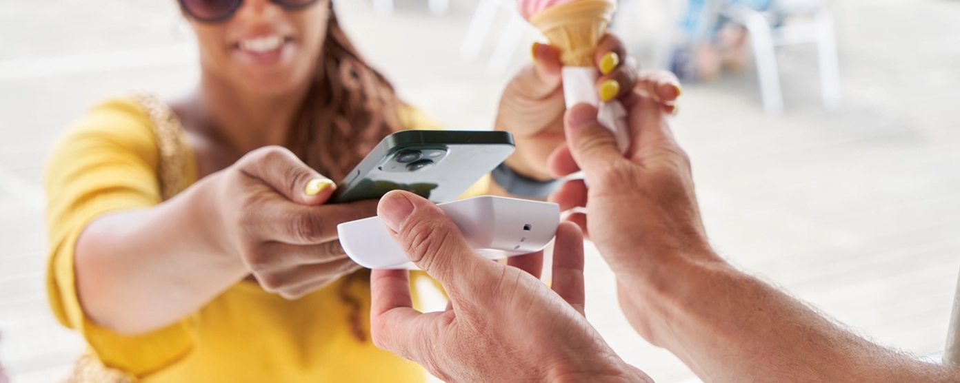 Close up of a smiling woman paying for an ice cream with her phone