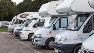 Row of motorhomes parked side by side at a campsite, angled front view with trees in background