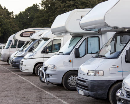 Row of motorhomes parked side by side at a campsite, angled front view with trees in background