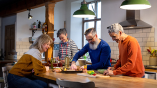 Group of friends cooking and laughing together in a cozy kitchen, preparing a shared meal