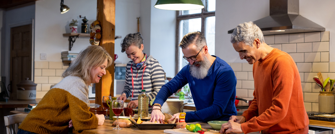 Group of friends cooking and laughing together in a cozy kitchen, preparing a shared meal