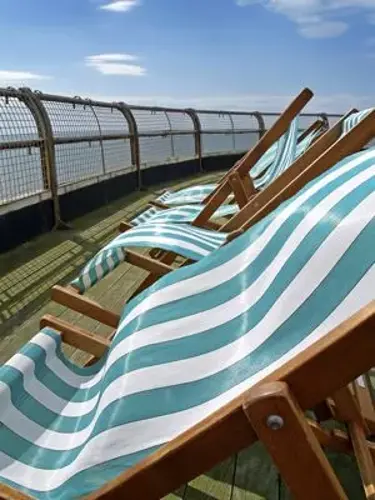 Row of empty striped teal and white deck chairs on a sunny outdoor deck with a railing and blue sky.