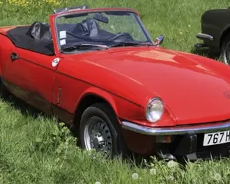 A red Triumph Spitfire 1500 convertible is parked on lush grass, highlighting its vintage charm and sporty appearance.