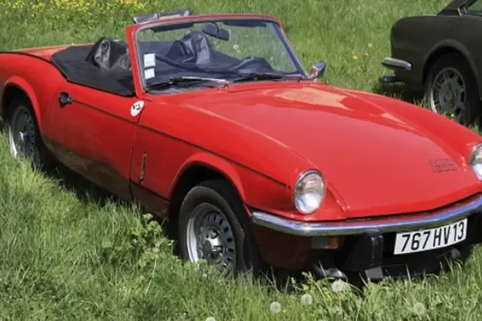 A red Triumph Spitfire 1500 convertible is parked on lush grass, highlighting its vintage charm and sporty appearance.