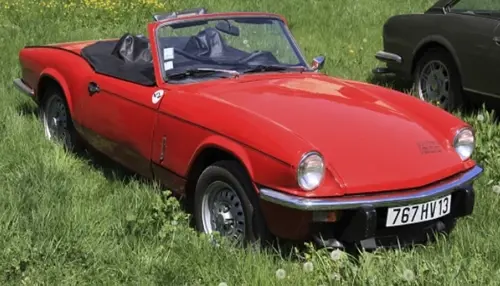 A red Triumph Spitfire 1500 convertible is parked on lush grass, highlighting its vintage charm and sporty appearance.