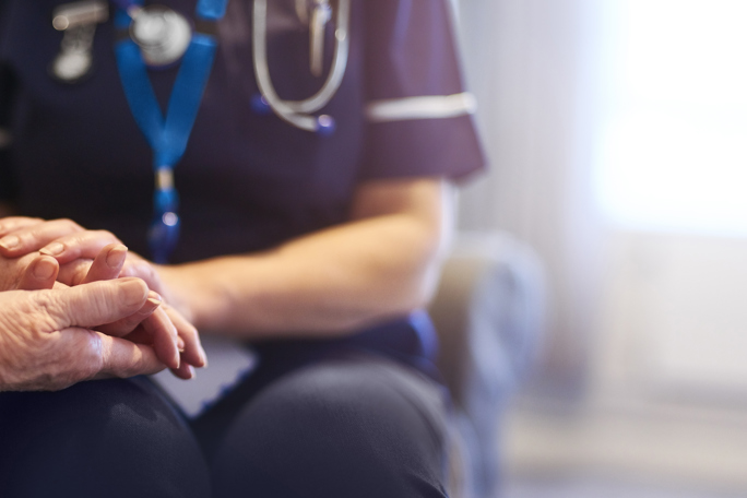 Nurse gently holding an elderly person’s hands, conveying care and support in a healthcare setting.