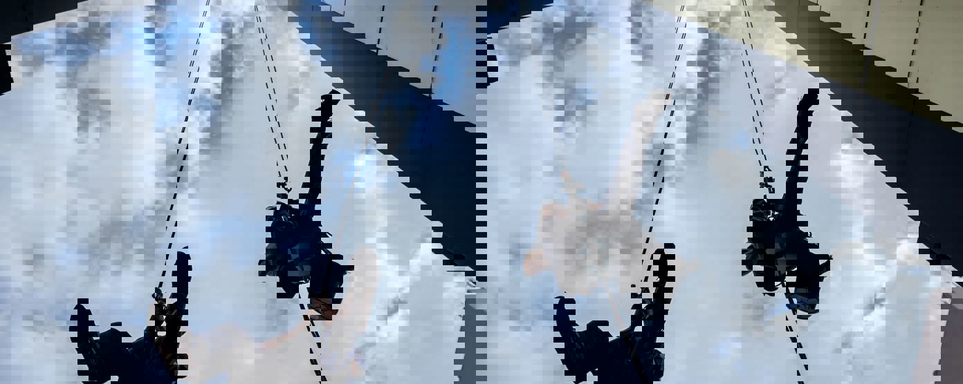 Silhouettes of two industrial climbers are washing, cleaning facade of a modern office building.