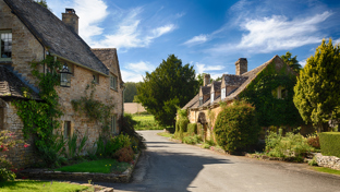 Village street with traditional stone cottages and green foliage under a blue sky.