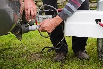 Close-up of hands connecting a 13‑pin trailer plug from a caravan to a car’s towbar socket on a grassy pitch