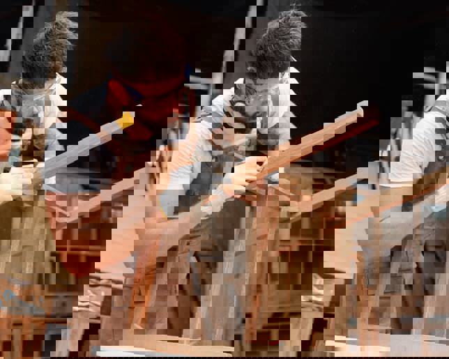 Young carpenter clear scrap wood on the chair in factory