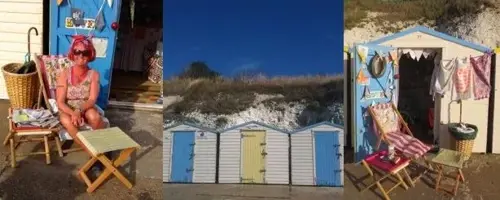 A row of colorful beach huts, one with a woman sitting outside on a deck chair. The huts are painted blue, yellow, and white, with bunting and summer decorations.
