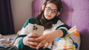 A young girl sitting on her bed using a mobile phone 