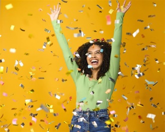 A lady smiles against a yellow background as gold confetti falls around her