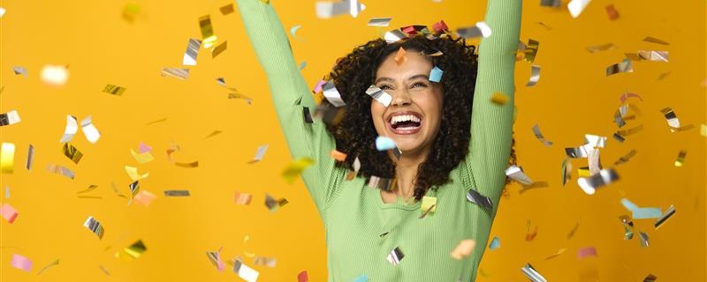 A lady smiles against a yellow background as gold confetti falls around her