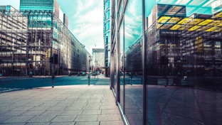 A bustling urban street with sleek glass commercial buildings mirroring the sky and adjacent architectural designs.