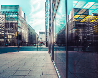A bustling urban street with sleek glass commercial buildings mirroring the sky and adjacent architectural designs.