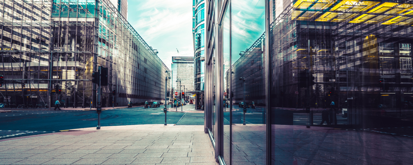 A bustling urban street with sleek glass commercial buildings mirroring the sky and adjacent architectural designs.