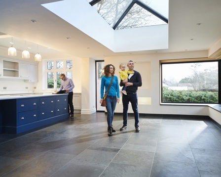 A young couple with a child tours a spacious, modern home with large windows and a skylight, while a real estate agent reviews documents.