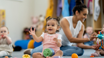 Toddlers sitting on a nursery floor with toys and an adult