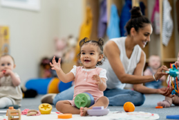 Toddlers sitting on a nursery floor with toys and an adult