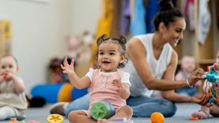Toddlers sitting on a nursery floor with toys and an adult