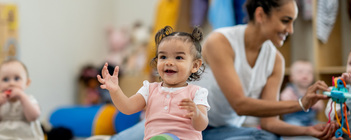 Toddlers sitting on a nursery floor with toys and an adult