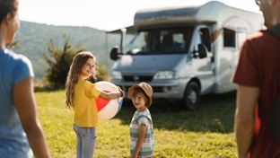 A girl holding a ball outside a camper van while her family smile on