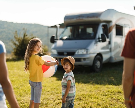 A girl holding a ball outside a camper van while her family smile on