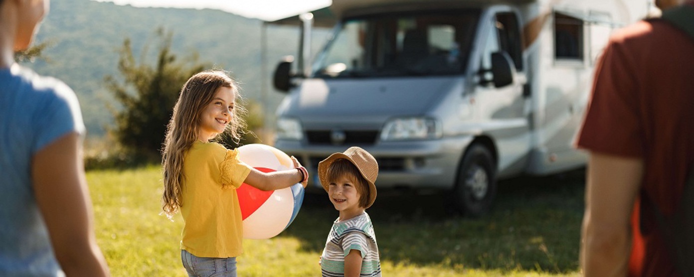 A girl holding a ball outside a camper van while her family smile on
