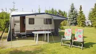Touring caravan with awning, table and floral garden chairs on a sunny campsite lawn for summer camping