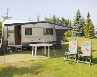 Touring caravan with awning, table and floral garden chairs on a sunny campsite lawn for summer camping