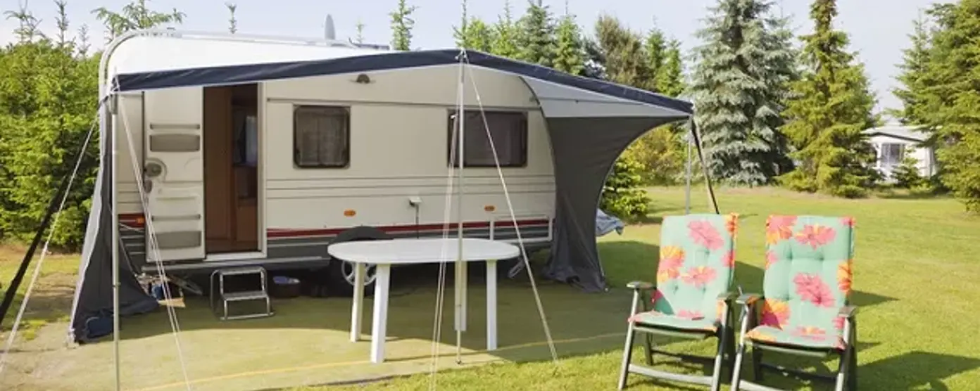 Touring caravan with awning, table and floral garden chairs on a sunny campsite lawn for summer camping