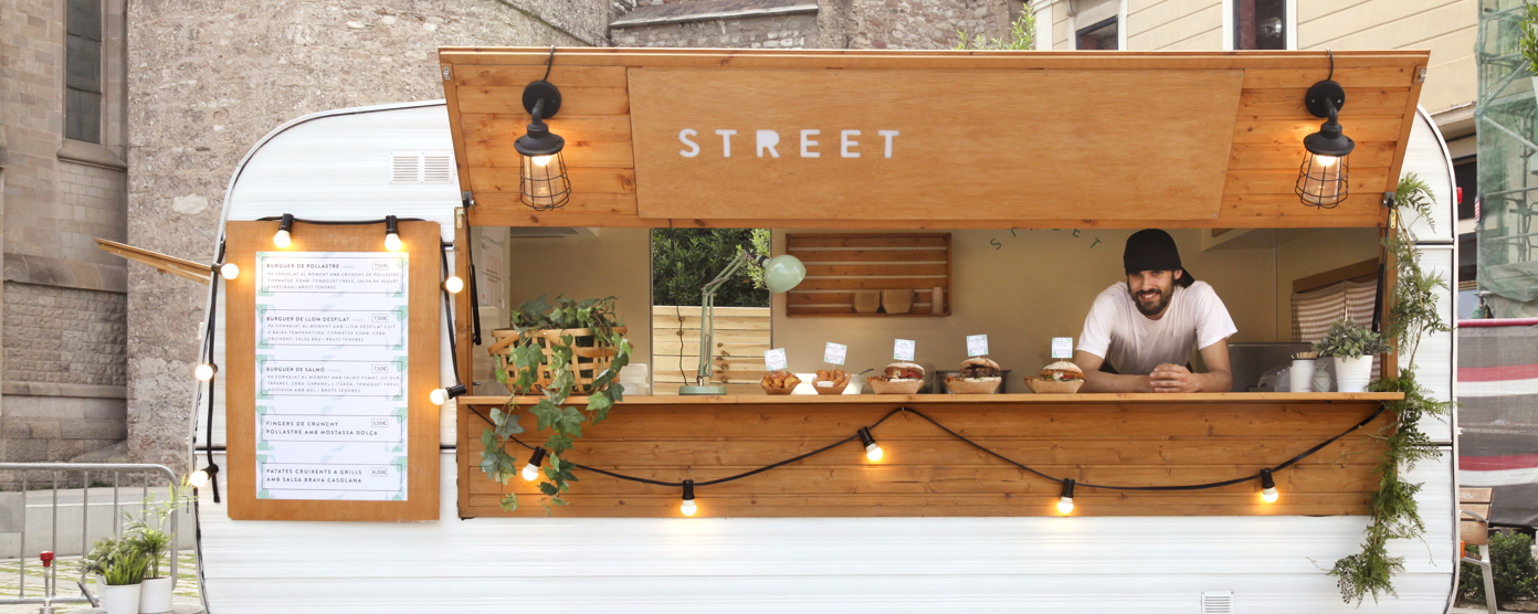 Vintage caravan converted into a street food truck with wooden serving hatch, string lights and a smiling vendor