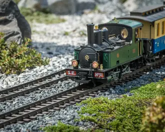 A green and black model train on a gravel track, with green foliage and rocks in the background