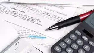 A close-up image of financial documents spread out on a desk, including printed forms, a black and red pen, and a calculator.