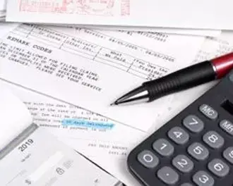 A close-up image of financial documents spread out on a desk, including printed forms, a black and red pen, and a calculator.