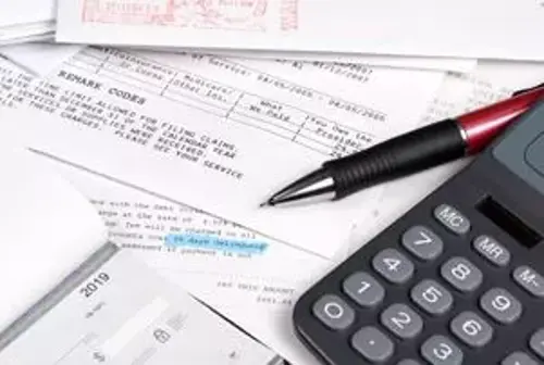 A close-up image of financial documents spread out on a desk, including printed forms, a black and red pen, and a calculator.