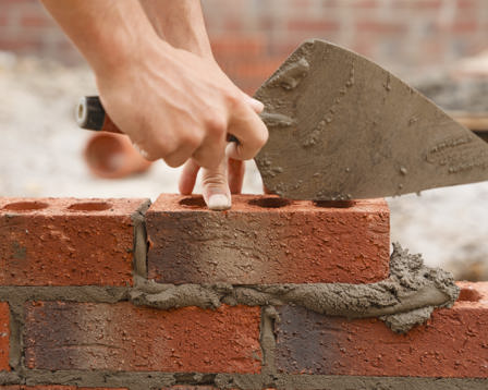 Bricklayer builder working laying red bricks and blocks on construction site