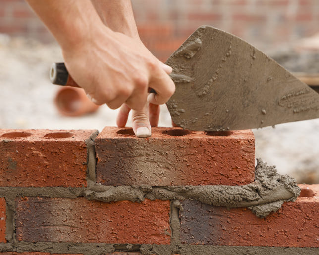 Bricklayer builder working laying red bricks and blocks on construction site