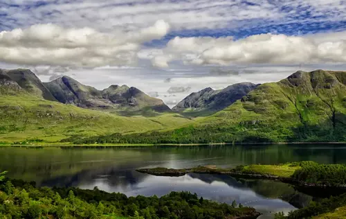 A stunning landscape featuring towering green mountains surrounding a calm lake with clear reflections.