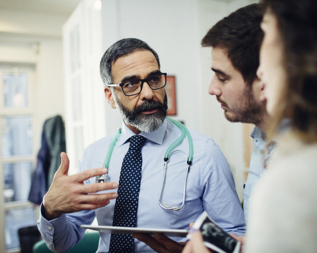 GP with stethoscope discussing test results with a couple during a clinic consultation