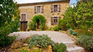 A traditional stone house with wooden shutters and surrounded by lush green foliage