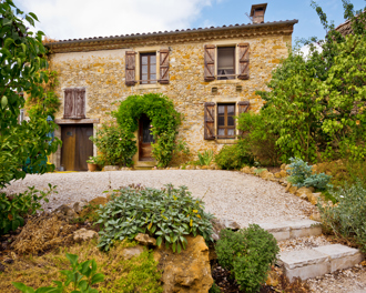 A traditional stone house with wooden shutters and surrounded by lush green foliage